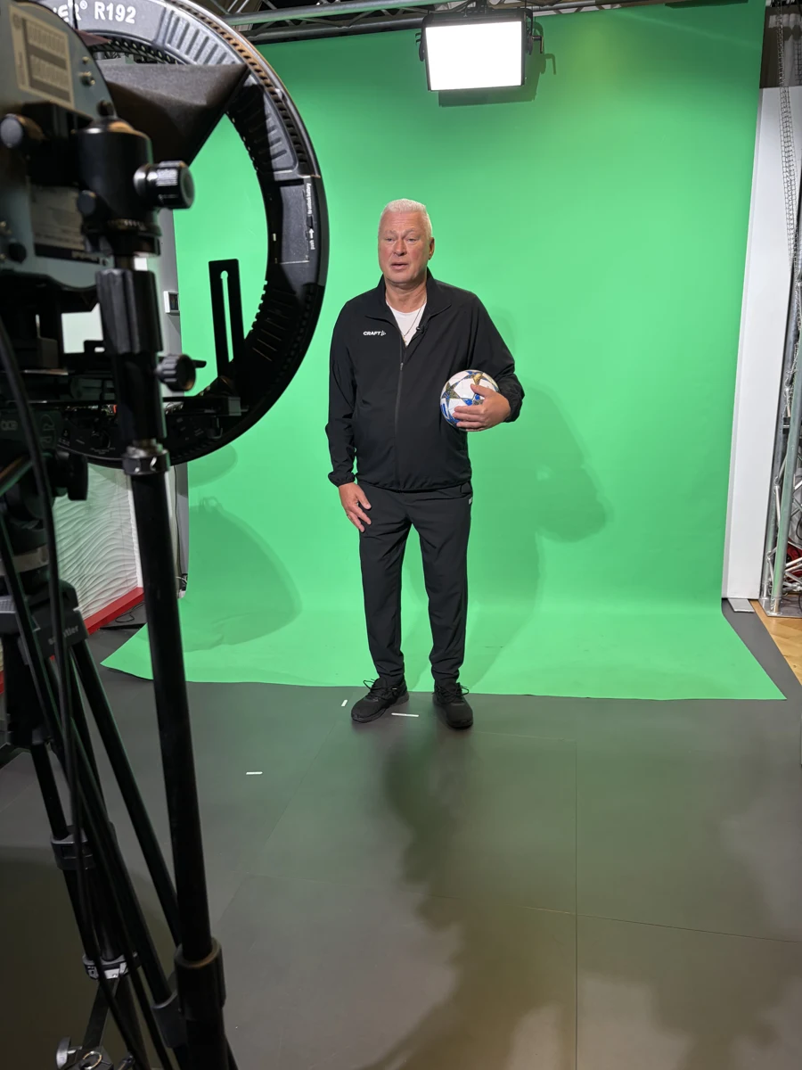 Kamera im Vordergrund und ein Mann mit Fußball vor einem Greenscreen