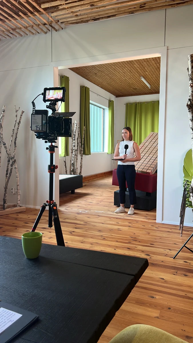 Eine Kamera filmt eine Frau mit Mikrofon in einem Raum mit Holzbalken