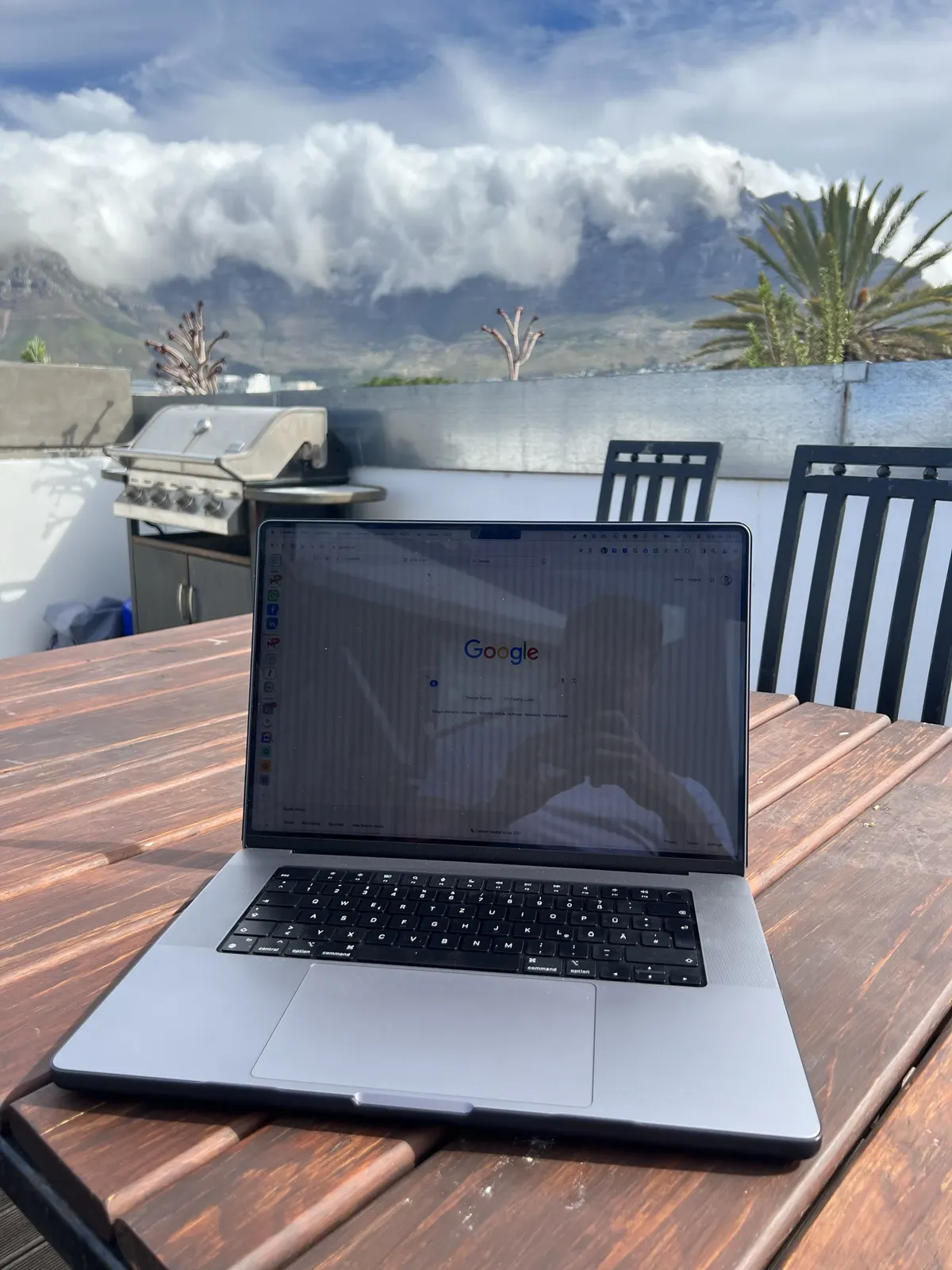 Laptop auf einem Tisch, dahinter ein Berg mit Wolken und Palmen